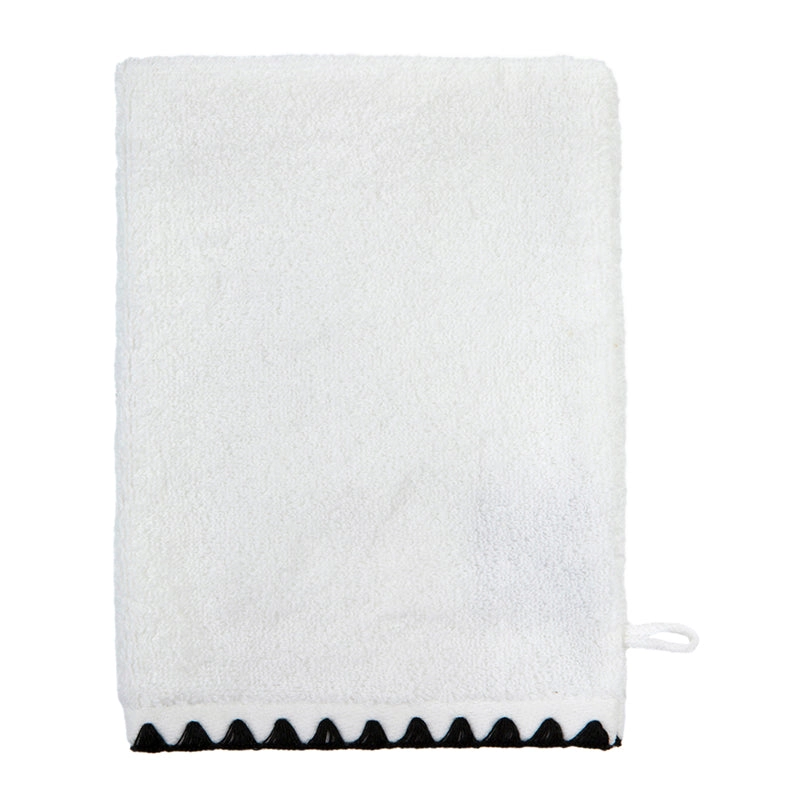 Guante de baño blanco visto de frente, con borde inferior en zigzag negro y un pequeño lazo lateral.