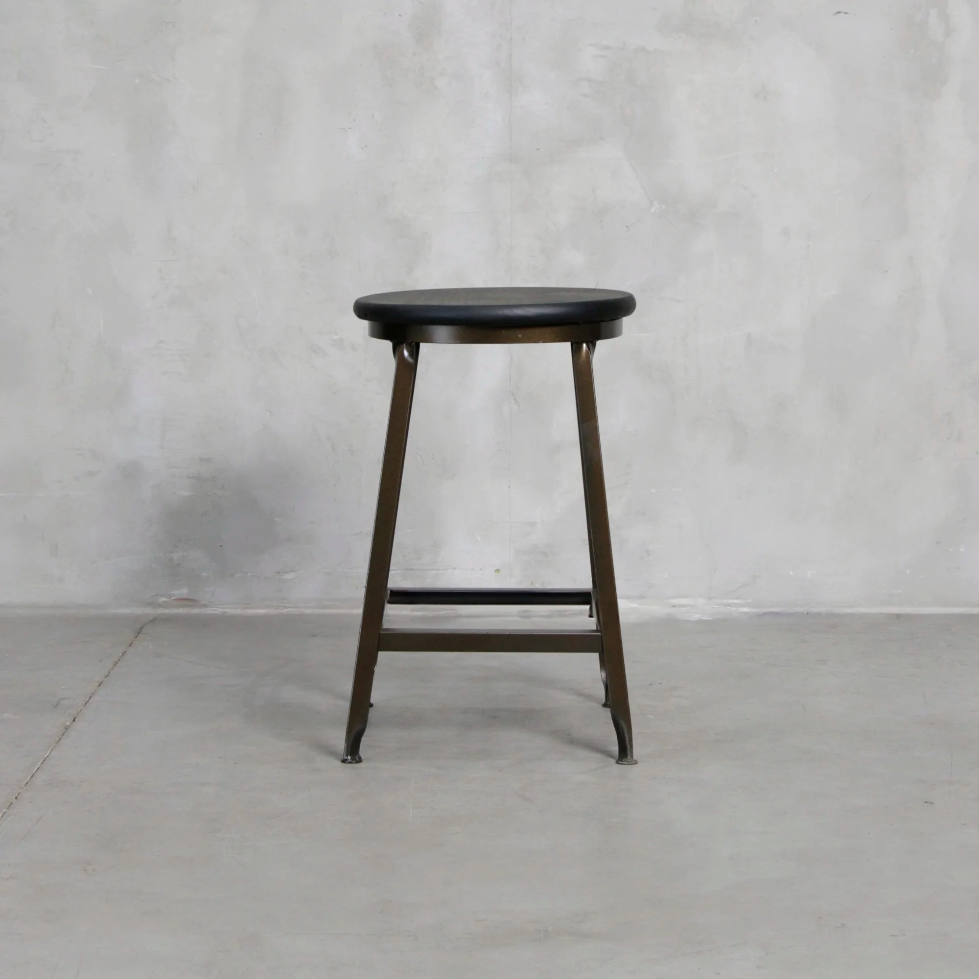 Taburete negro visto de frente, con asiento redondo y estructura metálica.