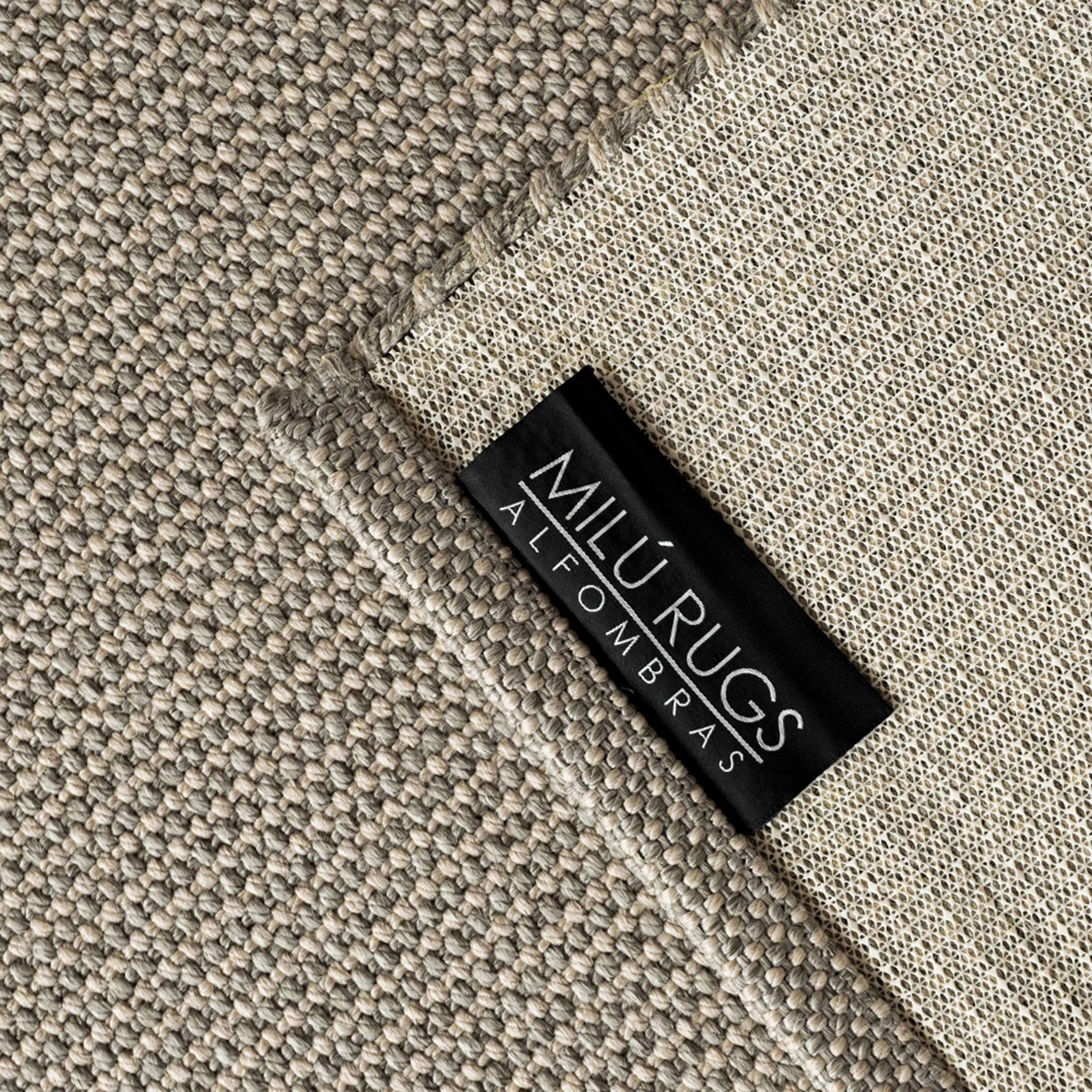 Detalle de la alfombra tejida en tonos beige y gris, con etiqueta Milú Rugs y vista de la base.